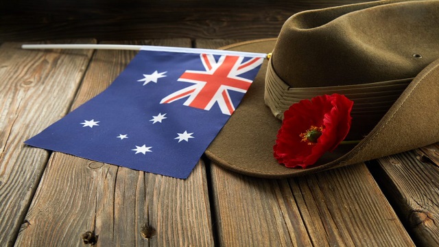 Australian army slouch hat and traditional ANZAC biscuits on dark recycled wood with remembrance red poppy and Australian flag